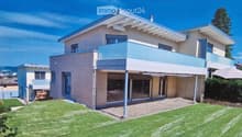 Modern two-story house with light-colored facade, large windows, and a spacious balcony overlooking the front yard.