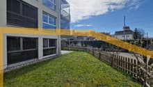 Well-maintained lawn with wooden fence, small tree, and modern house with large windows and balcony in the background.