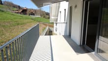 Balcony with a metal railing, covered by a retractable awning, overlooking a green hillside with scattered houses.