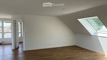 Completely empty room with wooden flooring, white walls, and large windows, including a skylight. No furniture or equipment.
