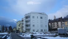 Multi-story residential building with balconies and windows, surrounded by other buildings and a snow-covered landscape.