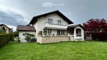 Two-story house with a stone base, white upper facade, multiple windows, and a well-maintained lawn.