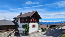House. Traditional Swiss house with red shutters, white walls, and a tiled roof, situated in a scenic mountain landscape.