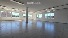 Empty room with tiled floor, white walls, large windows, and a central column. No furniture or equipment present.