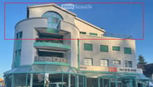 Modern multi-story building with curved facade, green shutters, balconies, and a Nissan dealership entrance.