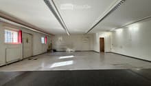 Empty room with white walls, concrete floor, fluorescent lighting, and a few windows. No furniture or equipment present.
