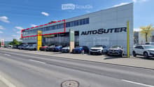 Modern car dealership building with large glass windows and signage for 'AUTOSUTER', several cars parked in front.