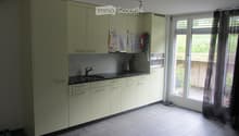 Kitchen. Modern kitchen with light-colored cabinets, a sink, an oven, and a window with a curtain. The floor is tiled, and there are some shoes near the window.