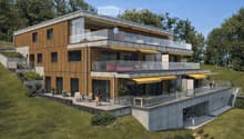 Modern two-story house with wooden and concrete exterior, multiple balconies, raised ground floor, and outdoor seating areas.