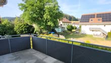 Balcony with metal railing overlooking a residential area with houses, trees, and a clear sky.
