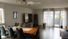 Modern dining area with a wooden dining table, six chairs, a television, a cabinet, and a potted plant near the sliding glass doors.