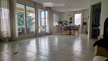Bright dining area with large windows and sliding glass doors leading to a balcony. The room features a dining table with chairs, a hanging light fixture, and a fireplace on the right side.