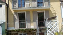 Two-story residential building with a balcony, wooden deck, and stairs leading to the entrance.