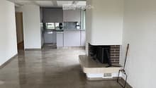 Empty living space with a fireplace, modern kitchen in the background, polished tile floor, and white walls.