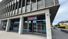 Modern commercial building entrance with large glass doors and a sign reading "LAKIMI III" above the entrance.