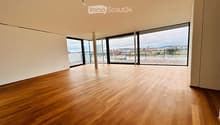 Empty room with wooden flooring, large windows, and a view of a river and cityscape.
