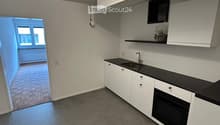 Modern kitchen with white cabinets, black countertop, sink, and oven. Open doorway leads to another room with brick flooring.