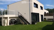 Modern two-story house with a raised ground floor, featuring a balcony, staircase, and outdoor grill area.