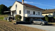 Two-story house with white exterior, brown roof, garage, and parking area.