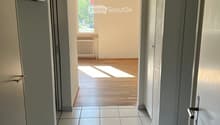 Empty hallway with tiled floor, white walls, and doors leading to other rooms. Natural light streams in from a window at the end.