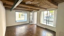 Empty room with wooden flooring, exposed wooden ceiling beams, large windows, and a door leading outside.