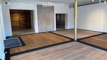 Empty room with wooden flooring, white walls, exposed ceiling beams, and a large wooden door in the background.