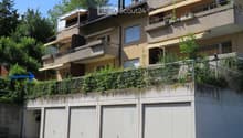 Multi-story residential building with balconies, awnings, and multiple garage doors at the base.