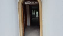 An arched entryway leads into a hallway with white walls and a wooden ceiling. The hallway is empty and has a smooth, light-colored floor.