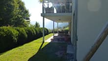 Garden area with a well-maintained lawn, wooden deck, potted plants, and a covered balcony area with outdoor furniture.