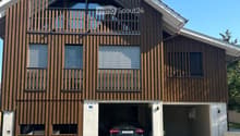 Modern two-story house with wooden facade, large garage, and balcony on the upper floor.