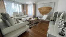 Modern living room with white leather sofas, a coffee table, a small side table, a hanging woven basket, and a decorative sculpture on a console table.