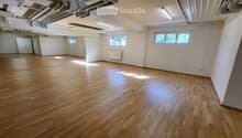 Empty room with wooden flooring, white walls, and large windows allowing natural light. No furniture or equipment present.