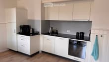 Modern kitchen with white cabinets, black countertops, and stainless steel appliances, including a coffee maker, oven, and sink.