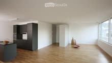 Modern kitchen with dark cabinets, light wooden flooring, and large windows. Includes a countertop with a bowl of fruit, vases, and a small decorative bowl.