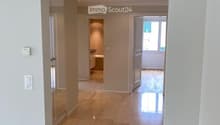 Bright hallway with beige tiled flooring, white walls, and recessed lighting. An open doorway leads to a bathroom with a visible bathtub and a windowed door to the outside.