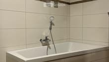 Modern bathroom with a bathtub, faucet, and showerhead. Light-colored tiles and a window provide natural light.