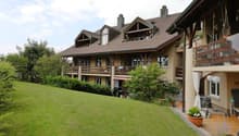 A two-story house with a tiled roof, multiple balconies, and a well-maintained garden with potted plants and a wooden deck.