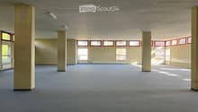 Empty room with carpeted floor, white walls, large windows, and pillars