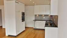 Modern kitchen with white cabinets, wooden flooring, stainless steel sink, and built-in oven.