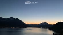 View from a balcony or terrace overlooking a serene lake with distant mountains during sunset.