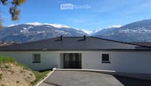 Modern white house, black roof, large windows, driveway, snowy mountains in the background