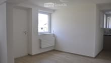 Empty room with wooden flooring, white walls, a window, a radiator, and a door. No furniture or equipment is present.