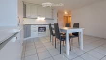 A modern, well-lit kitchen and dining area with white cabinets, a stove, refrigerator, and a dining table with chairs.