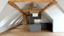 Modern kitchen with wooden beams, light wooden flooring, grey cabinets, and a central island.