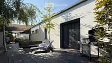 Wooden deck area with a modern house in the background, featuring a grill, lounge chairs, a small table, and a sofa.