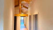 Wooden hallway with exposed wooden beams and recessed lighting, leading to an open area with a view of a balcony.