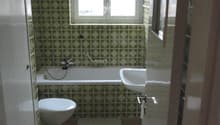 Bathroom with green patterned tiles, bathtub, toilet, sink, and a window above the bathtub.