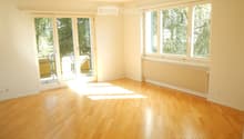 Empty room with light wooden flooring, large windows, and sliding glass doors leading to a balcony.