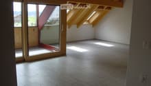 Empty room with exposed wooden beams, tiled floor, large sliding glass door leading to a balcony, and skylights allowing natural light.