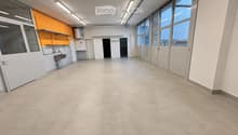 Empty room with white walls, large windows, and a sink area in the corner. No furniture or equipment present.